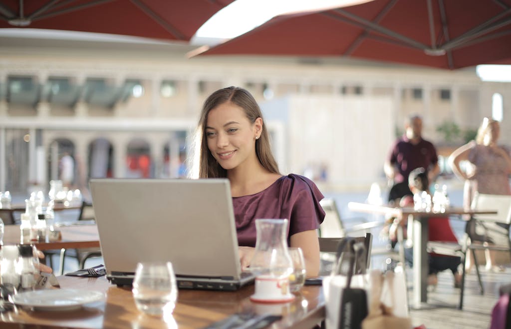 Woman in Purple Shirt Sitting by the Table Using Macbook