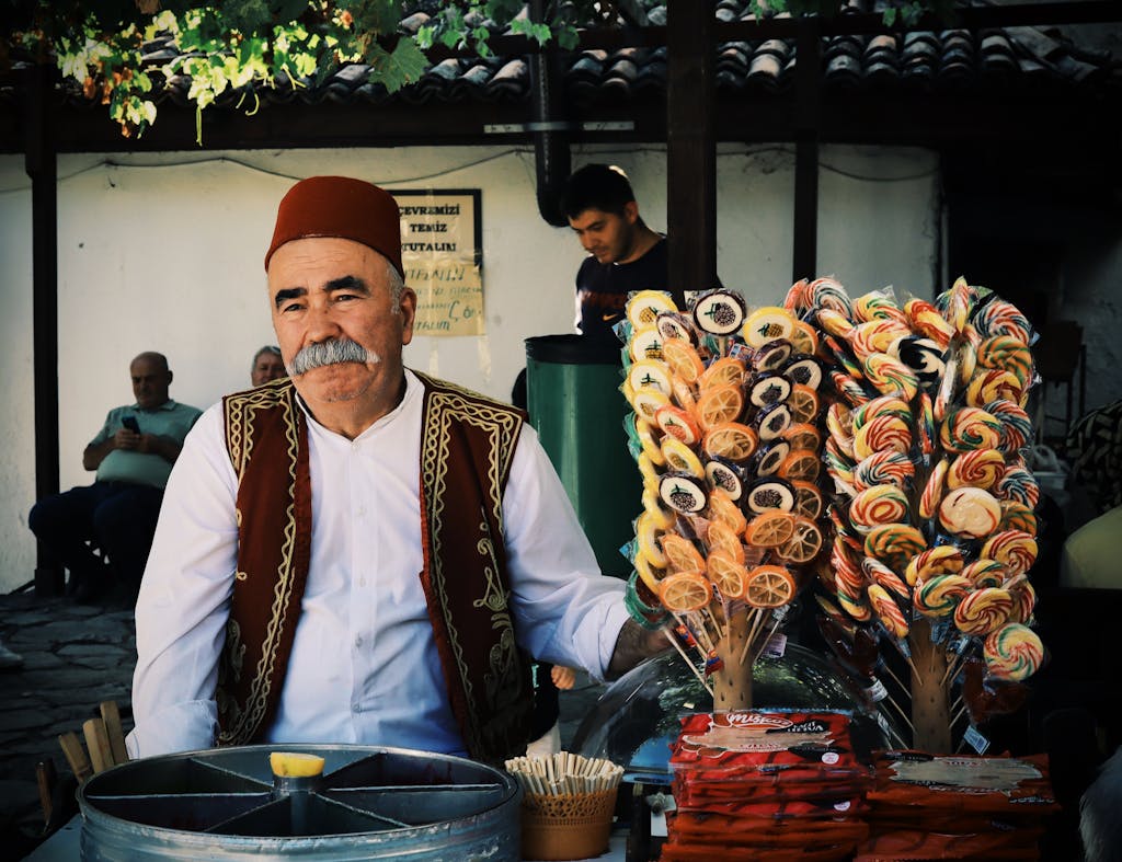 Elderly Merchant with Fez Hat Standing by Stall with Lollipops on Street in Turkish City