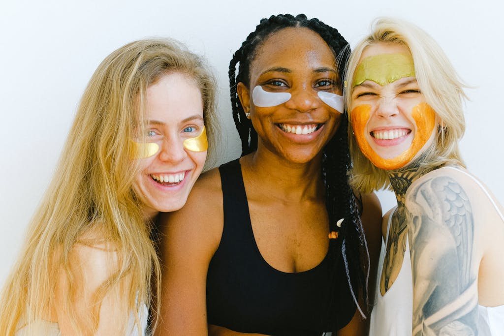 Group of women with masks and patches smiling while looking at camera and laughing during skincare procedure in studio on weekend