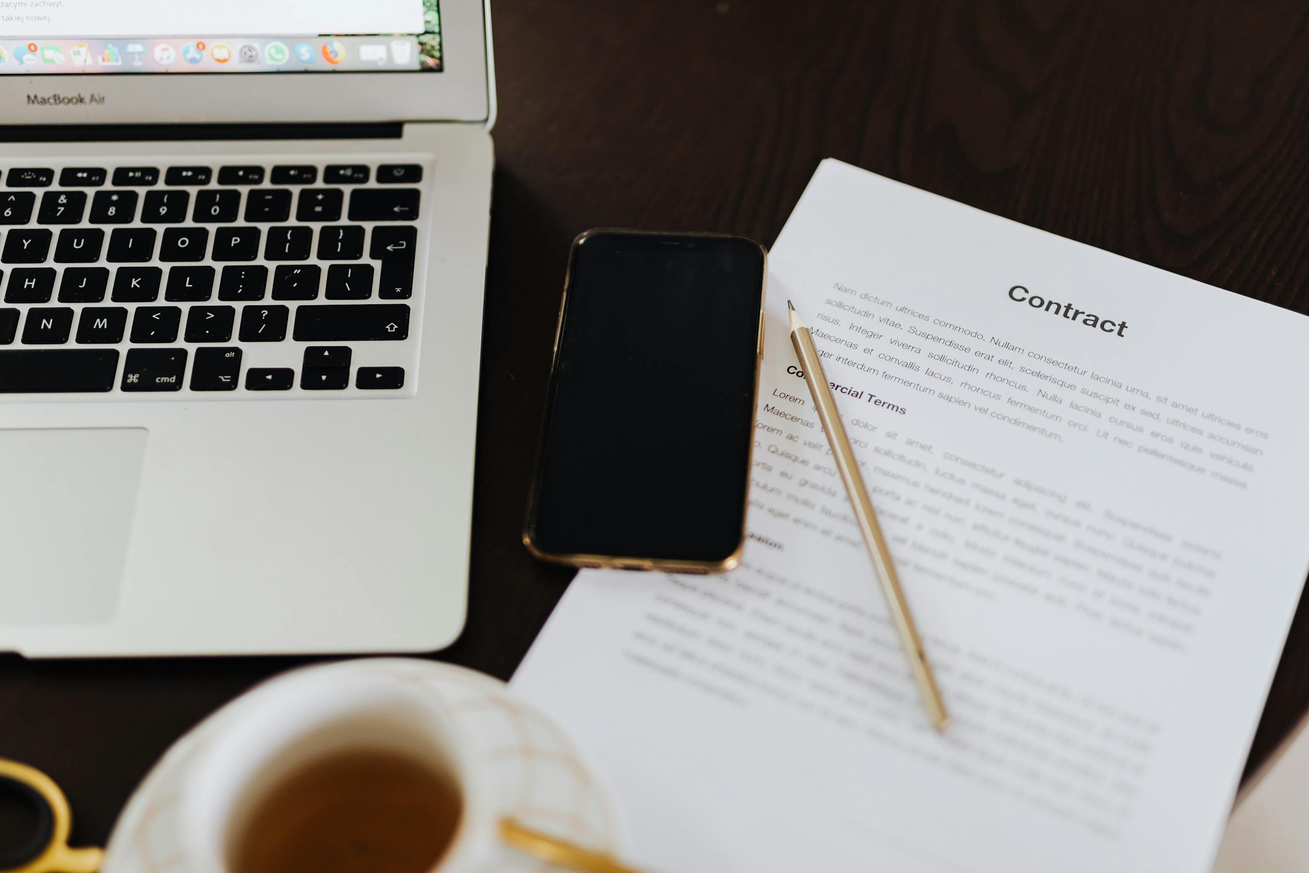 Laptop, Smartphone and a Contract Document Lying on the Desk 