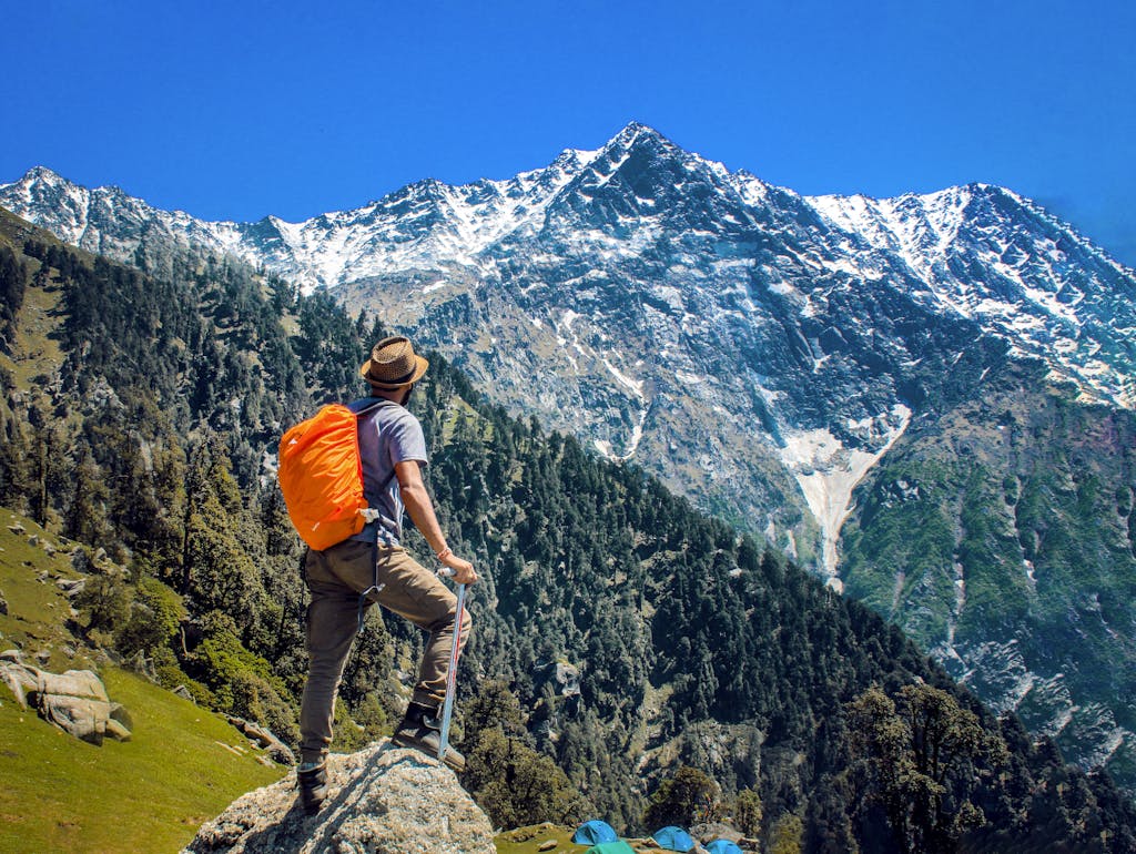 Man Wearing Blue Shirt Standing on Cliff While Watching Mountain