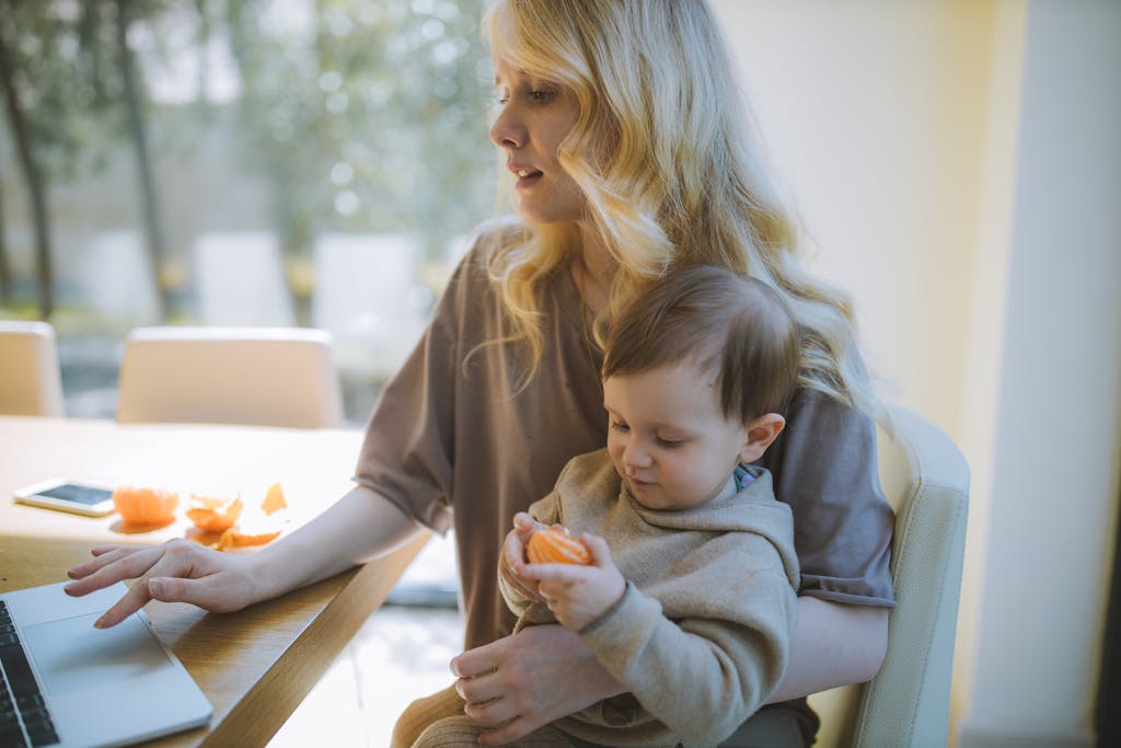 Photo Of Woman Digital Nomad Carrying Her Baby While Working On Her Laptop