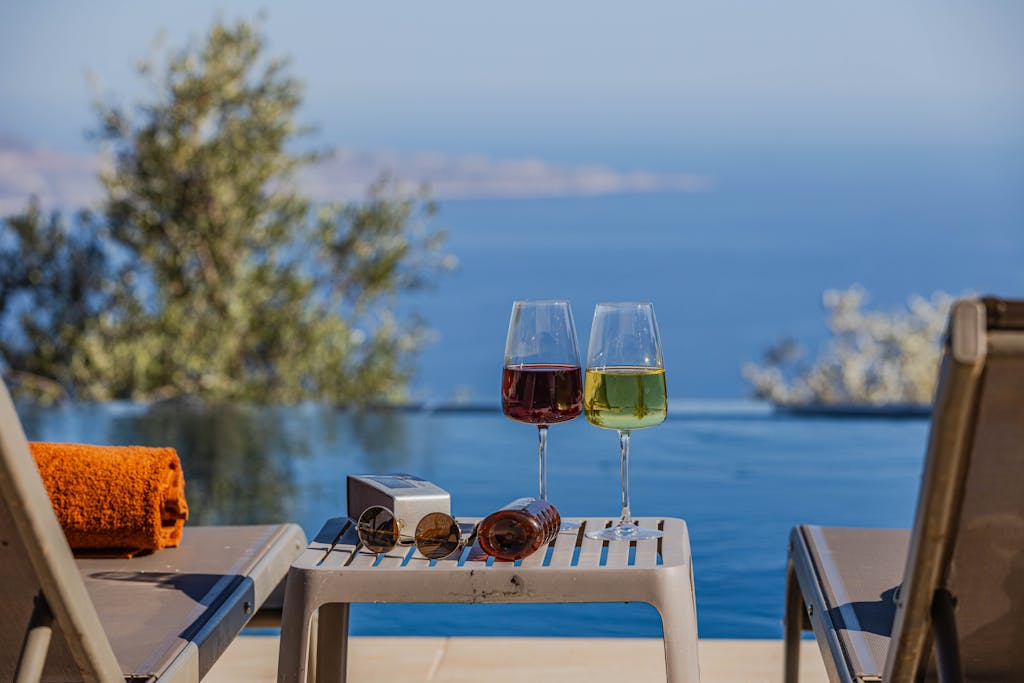 Two glasses of wine sit on a table next to a pool